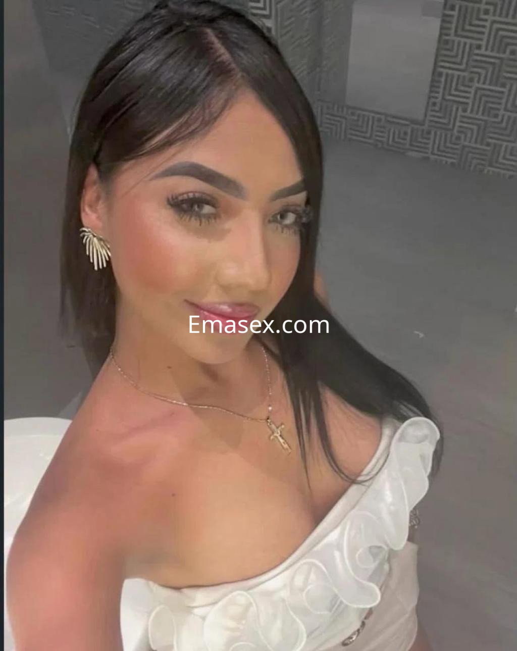 Escort en Las Palmas con cabello largo y lacio, luciendo un top blanco con detalles, en un entorno moderno.