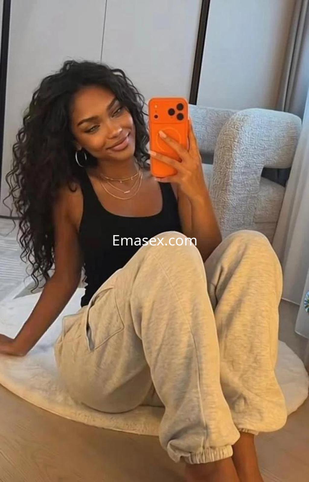 Puta con cabello rizado y oscuro, vestida con camiseta negra y pantalones grises, posando en Girona.
