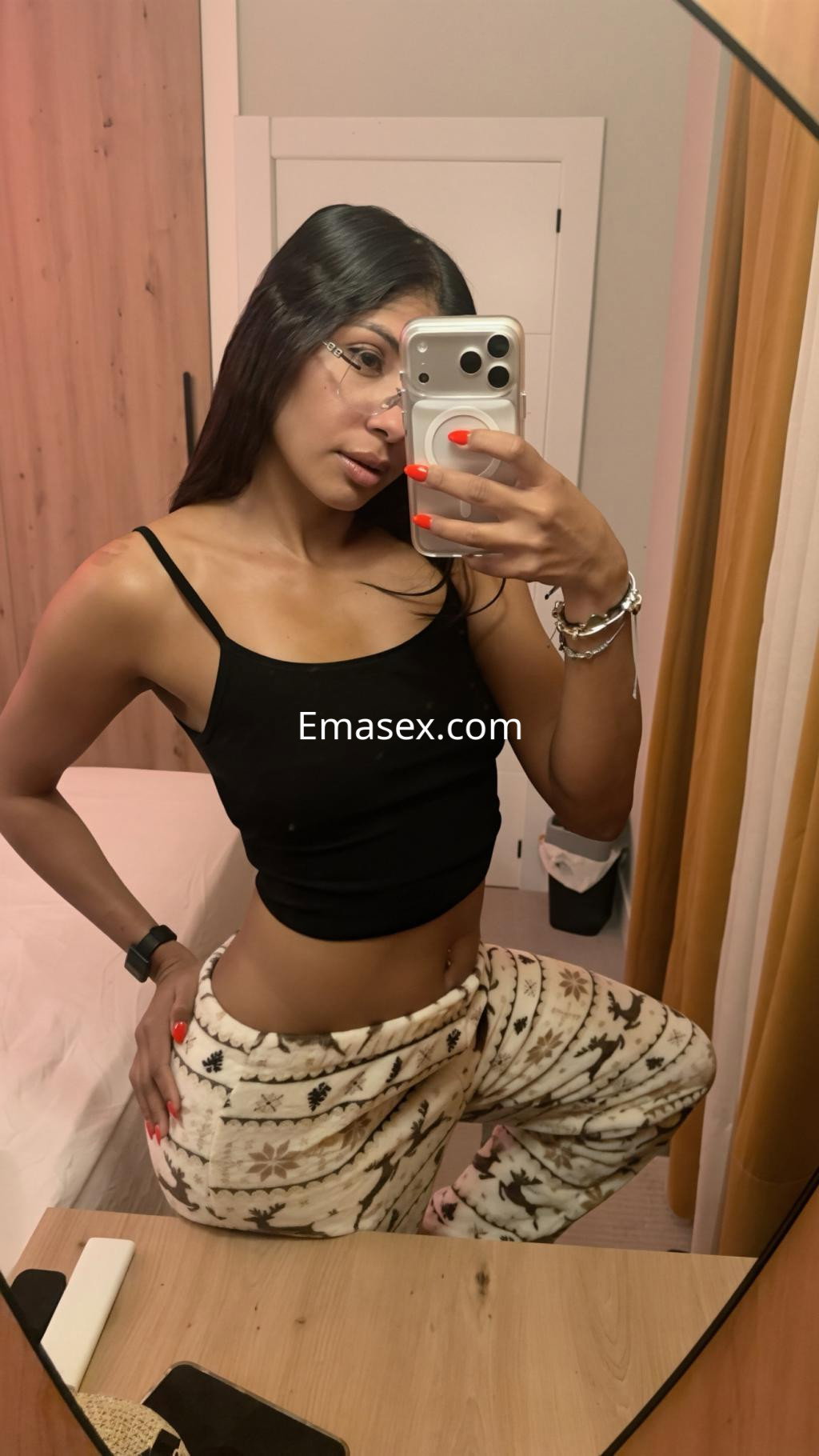 Escort en Santander, posando frente a un espejo con un top negro y pantalones de pijama claros, mostrando su figura.