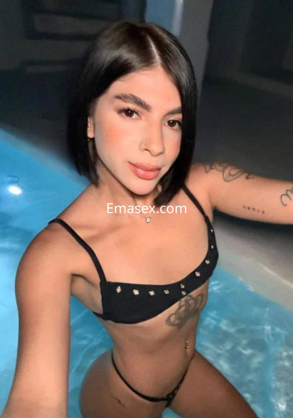 Escort en Palma de Mallorca posando en una piscina con un bikini negro adornado y un peinado lacio.