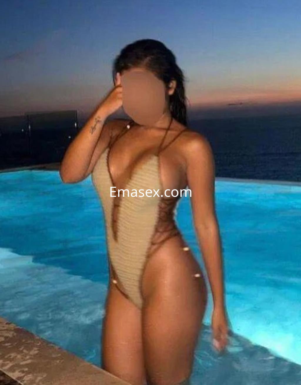 Escort en Toledo, posando junto a una piscina al atardecer, luciendo un bañador de corte profundo y detalles de cuerda.