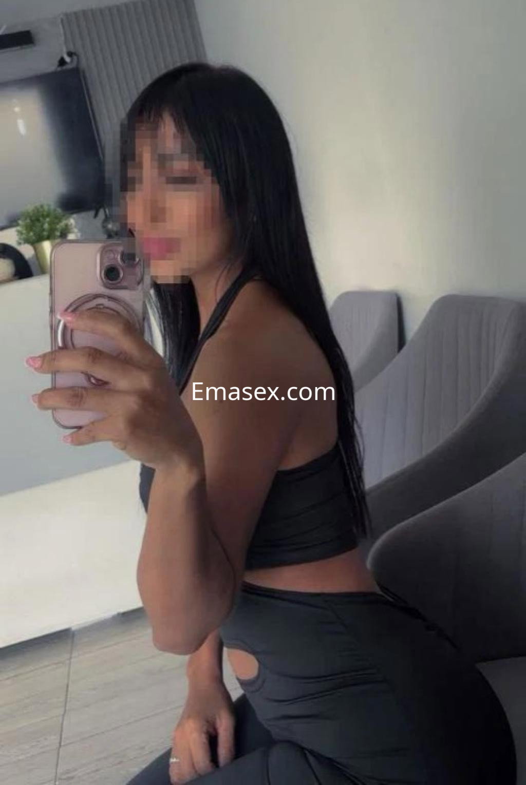 Escort en Valencia posando con un top negro y pantalones ajustados, mientras se toma una selfie en interiores.