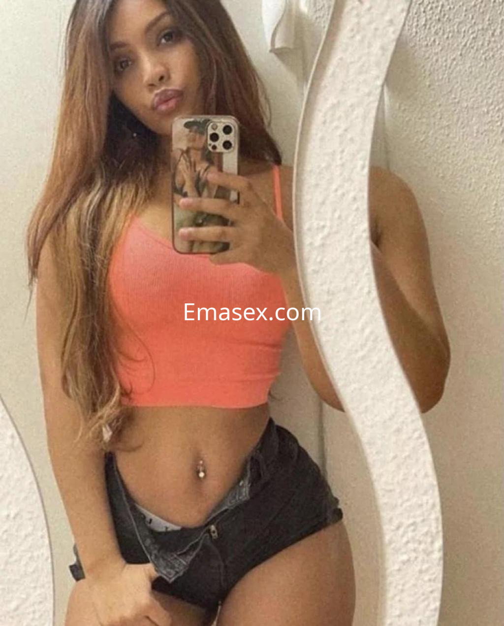 Escort en Zamora con cabello largo y lacio, viste una blusa ajustada de color naranja y shorts oscuros.
