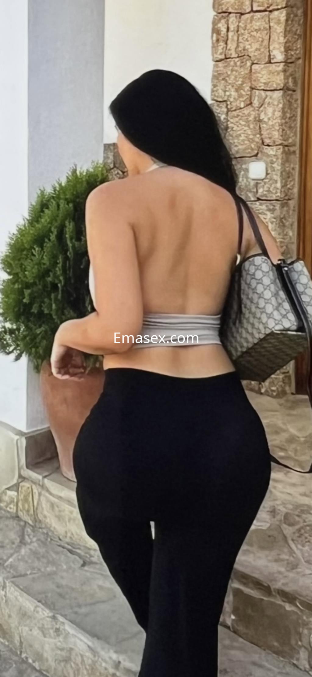 Puta de espaldas, con top gris y pantalones negros, caminando hacia una entrada en Donosti.