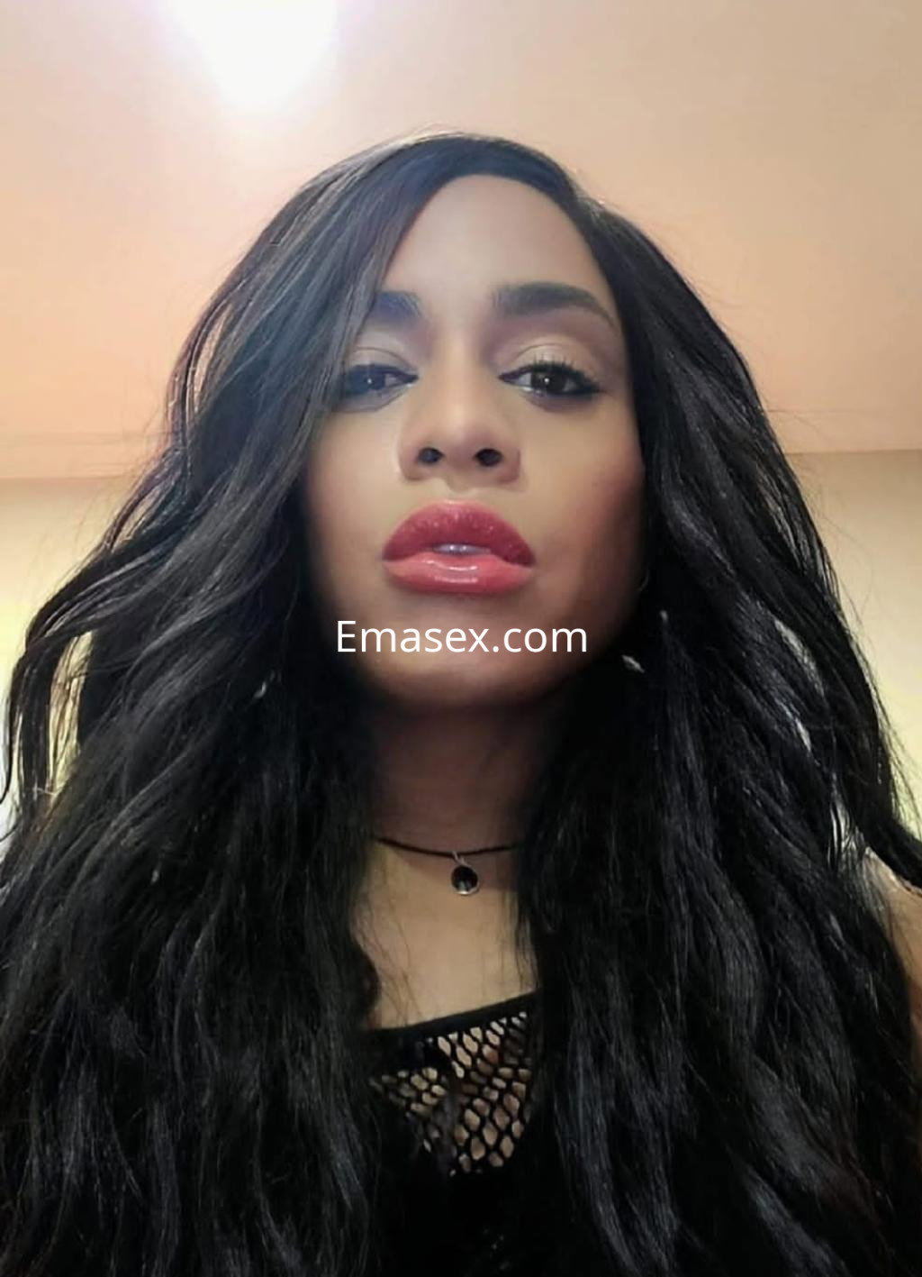 Puta trans con cabello largo y ondulado, viste una blusa negra y muestra un maquillaje llamativo en Santander.