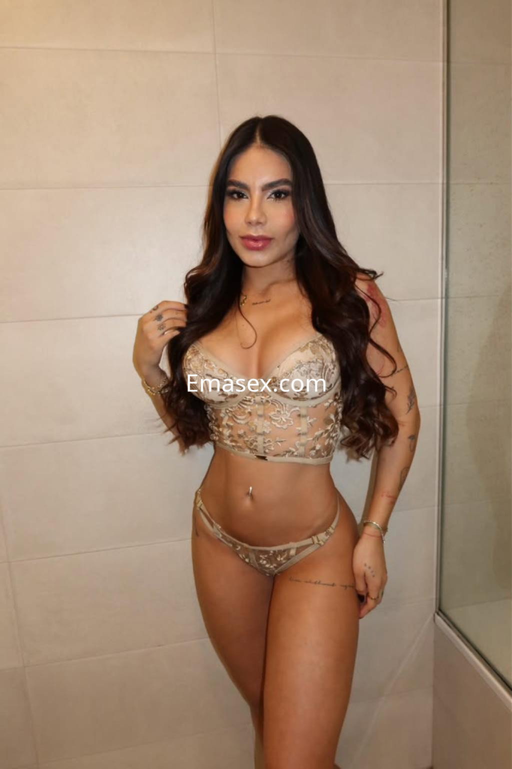Puta en Vitoria posa en un baño, vistiendo un conjunto de lencería beige con detalles, luciendo cabello largo y suelto.