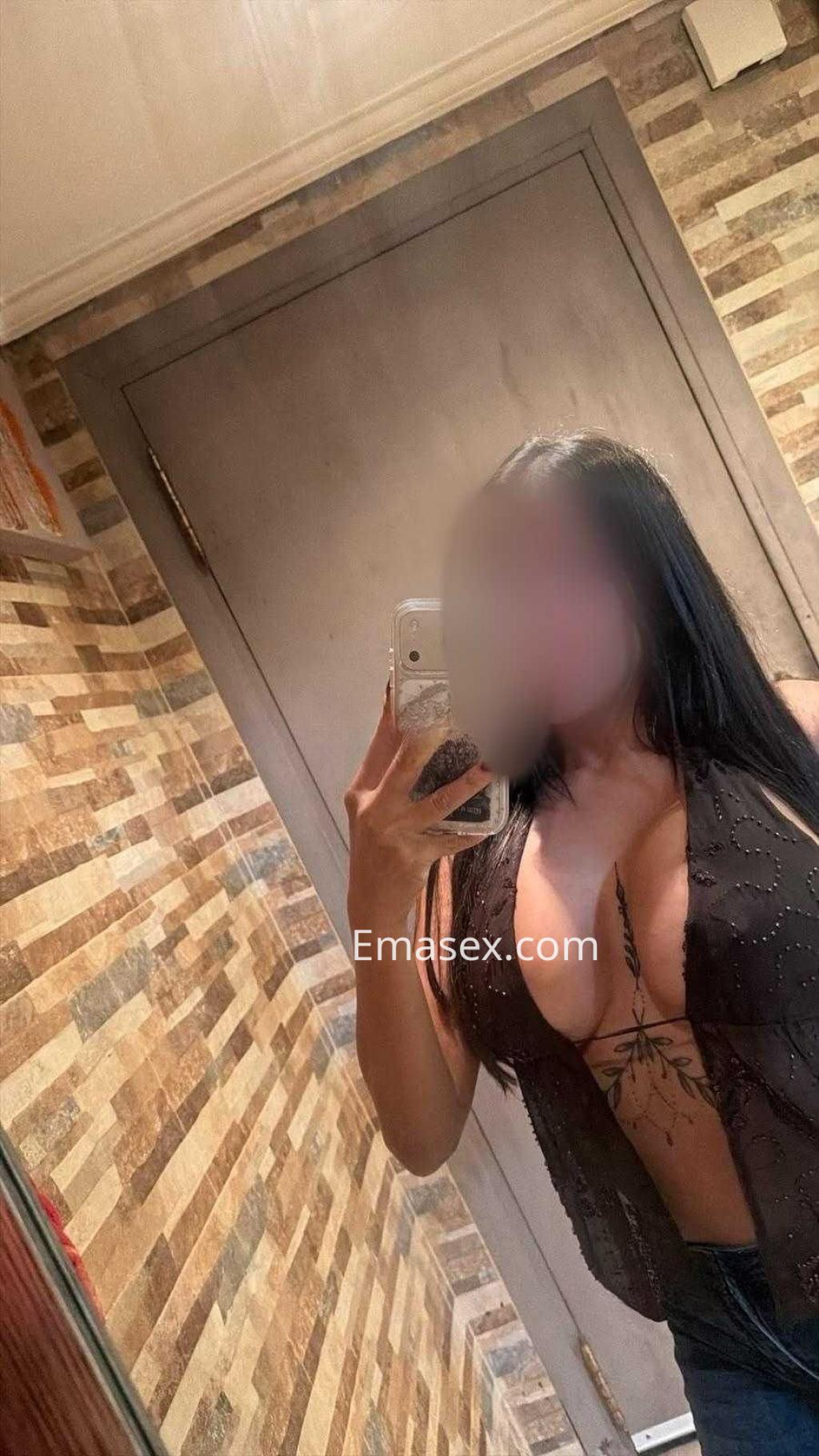 Puta en Lugo posando con una blusa transparente que resalta su figura, frente a un fondo de azulejos.
