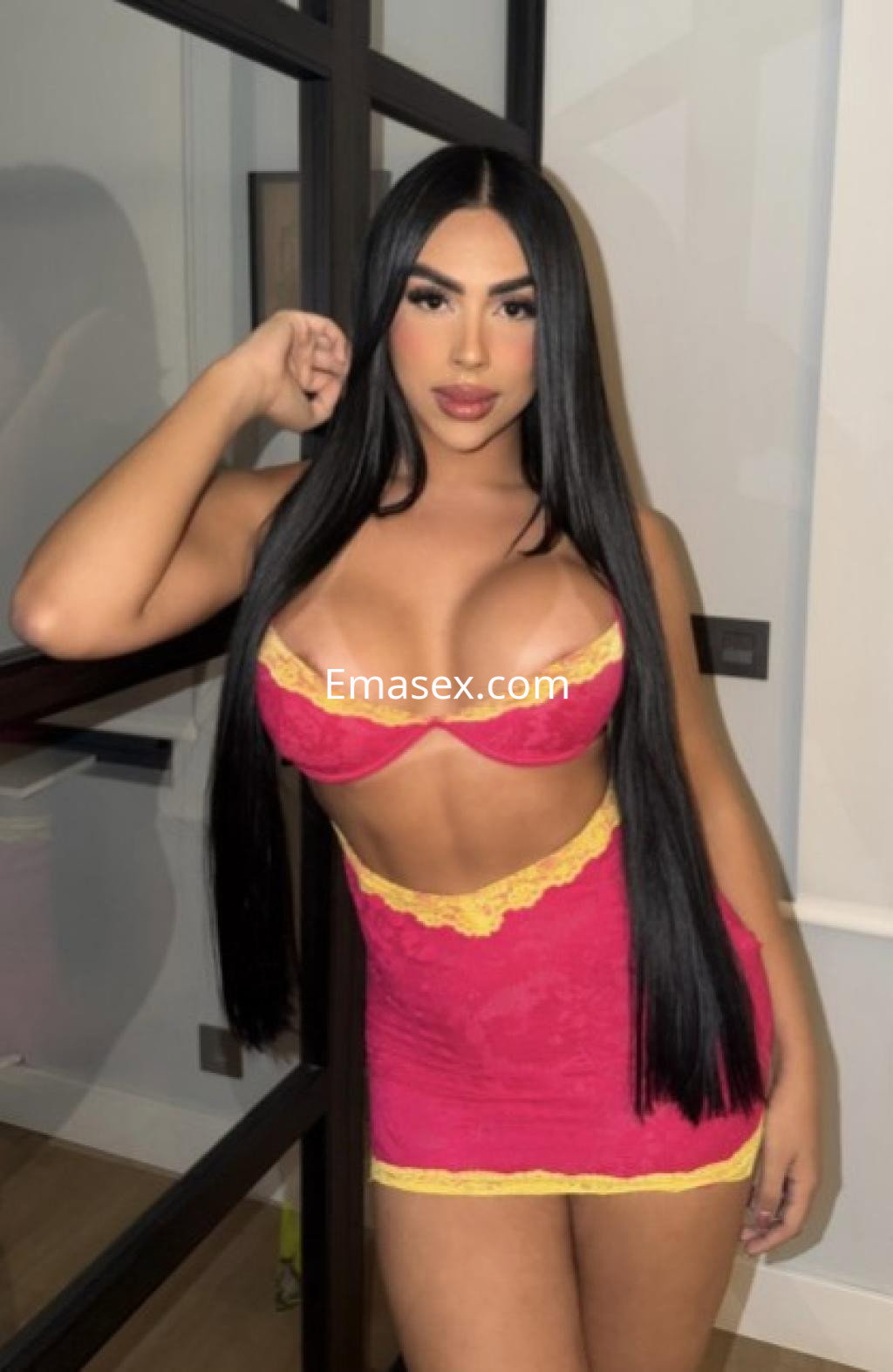 Escort trans en Vitoria con cabello largo y lacio, vistiendo un conjunto de lencería rosa con detalles amarillos.