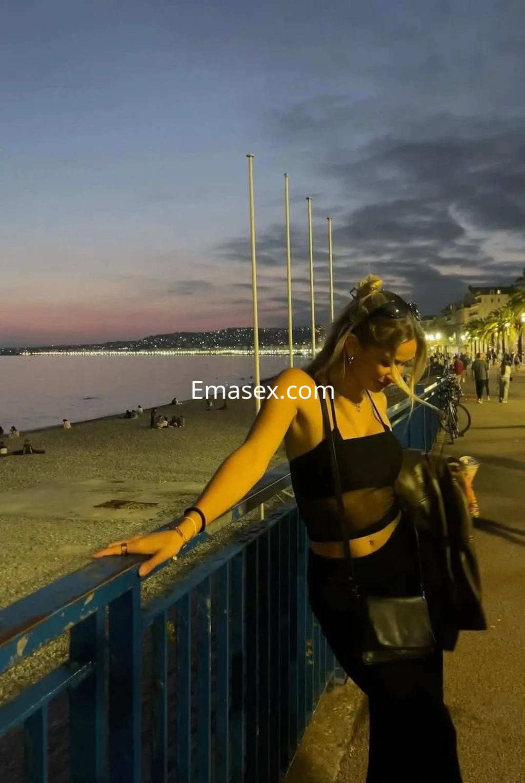 Escort en Valencia, luciendo un top negro y falda larga, posando junto a la playa al atardecer.