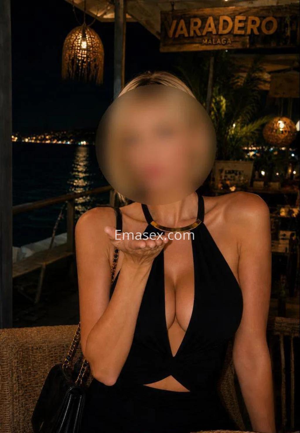 La puta viste un vestido negro ajustado con escote pronunciado, posando en un ambiente nocturno en Lleida.