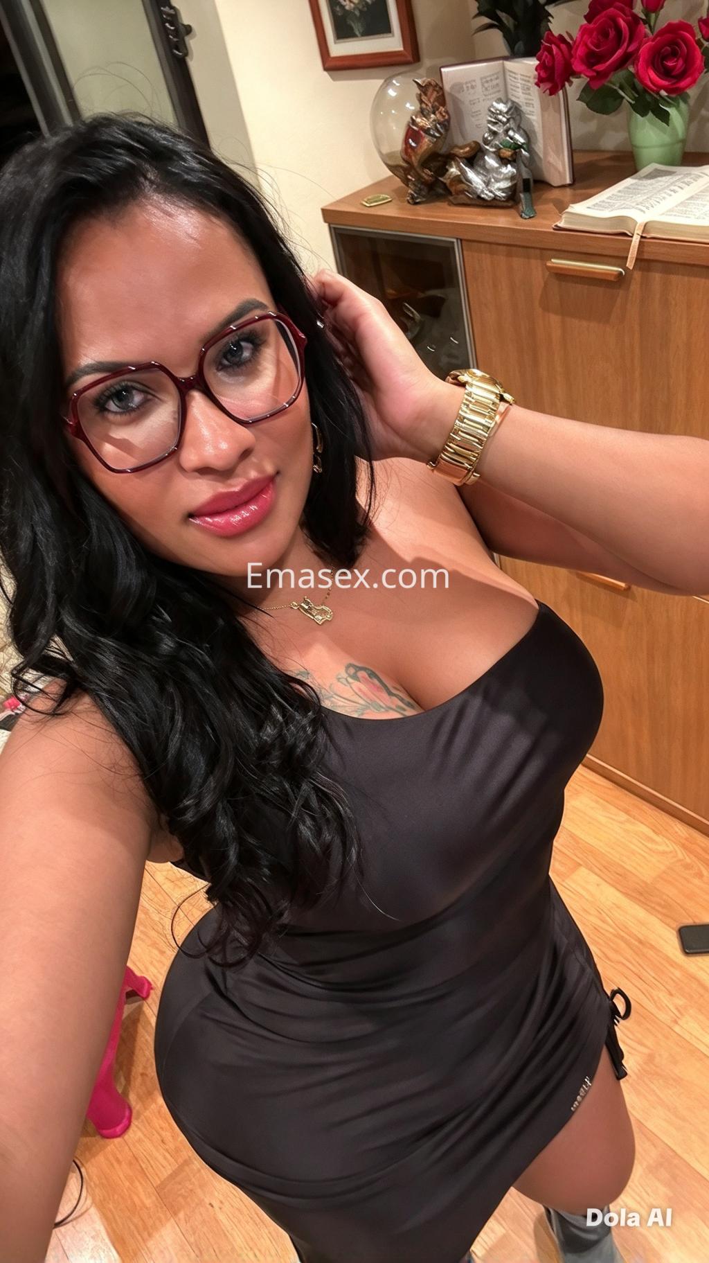 Escort trans en Logroño con cabello largo y oscuro, usando un vestido negro ajustado y gafas, sonríe en un ambiente interior.