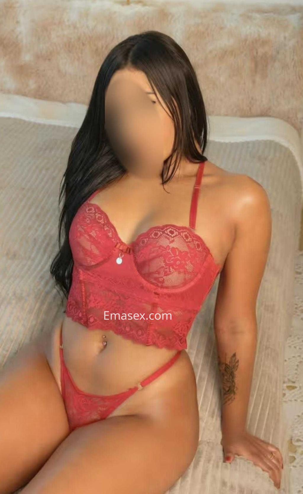 Escort en Madrid vistiendo lencería roja de encaje, con cabello largo y lacio, sentada en una cama.