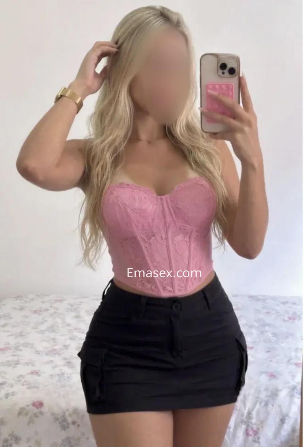 Escort en Madrid posando frente a un espejo, con un corset rosa y una falda corta negra.