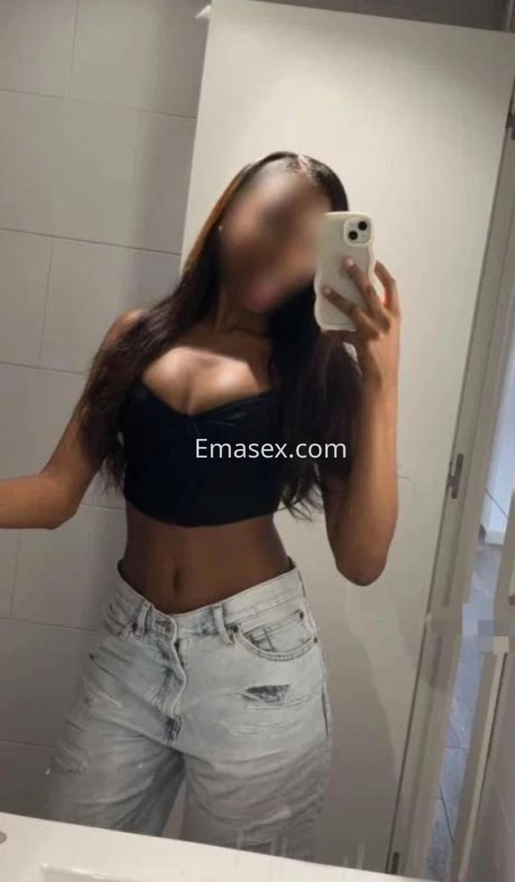 La escort en Lugo se toma una selfie en el espejo, vistiendo un top negro y jeans ajustados claros.