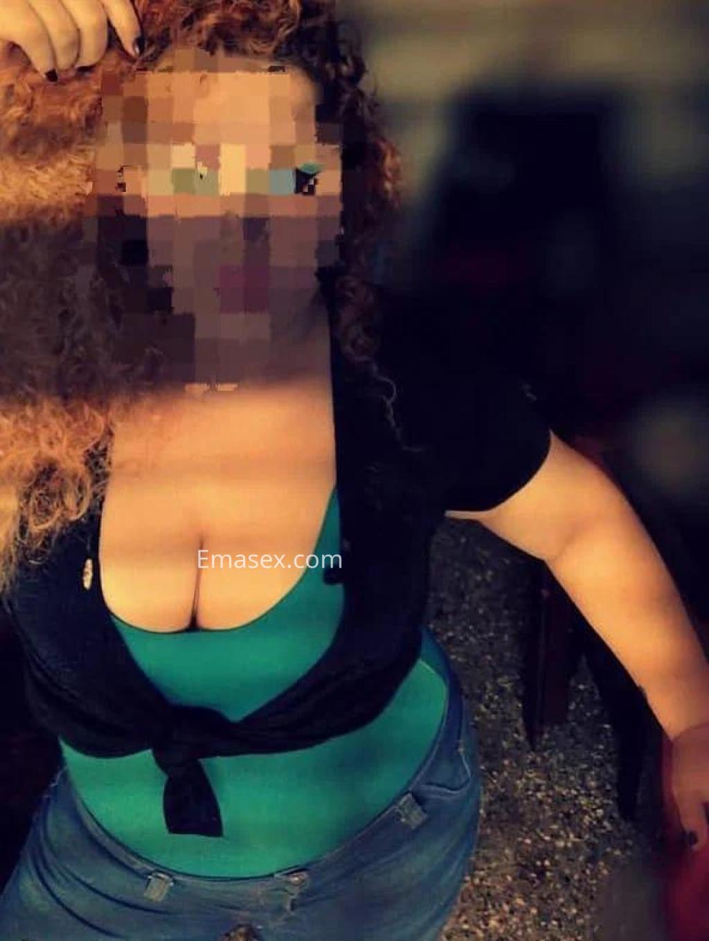 Escort en Pontevedra con cabello rizado y rubio, vistiendo una blusa verde y jeans ajustados, posando de lado.
