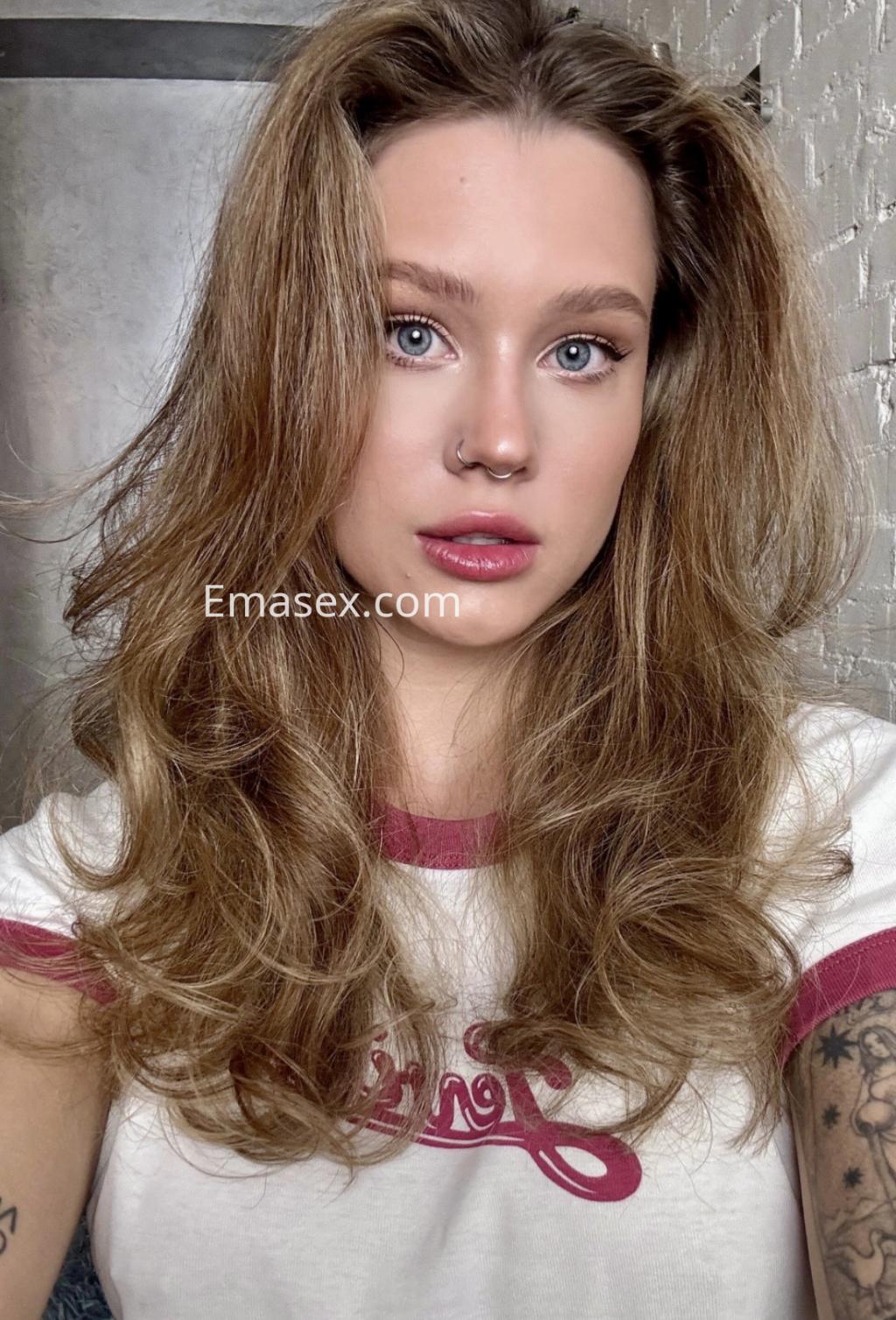 Escort en Alicante con cabello rizado y rubio, lleva una camiseta blanca con detalles en rojo y luce un maquillaje natural.