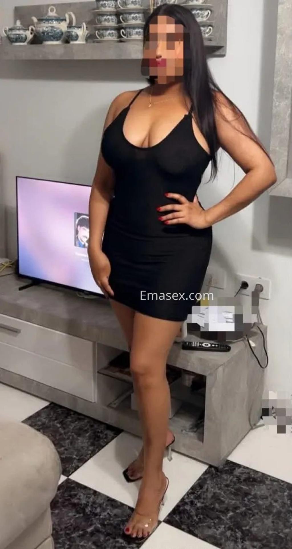 Escort en Madrid luciendo un vestido negro ajustado y sandalias transparentes, posando en un ambiente moderno.