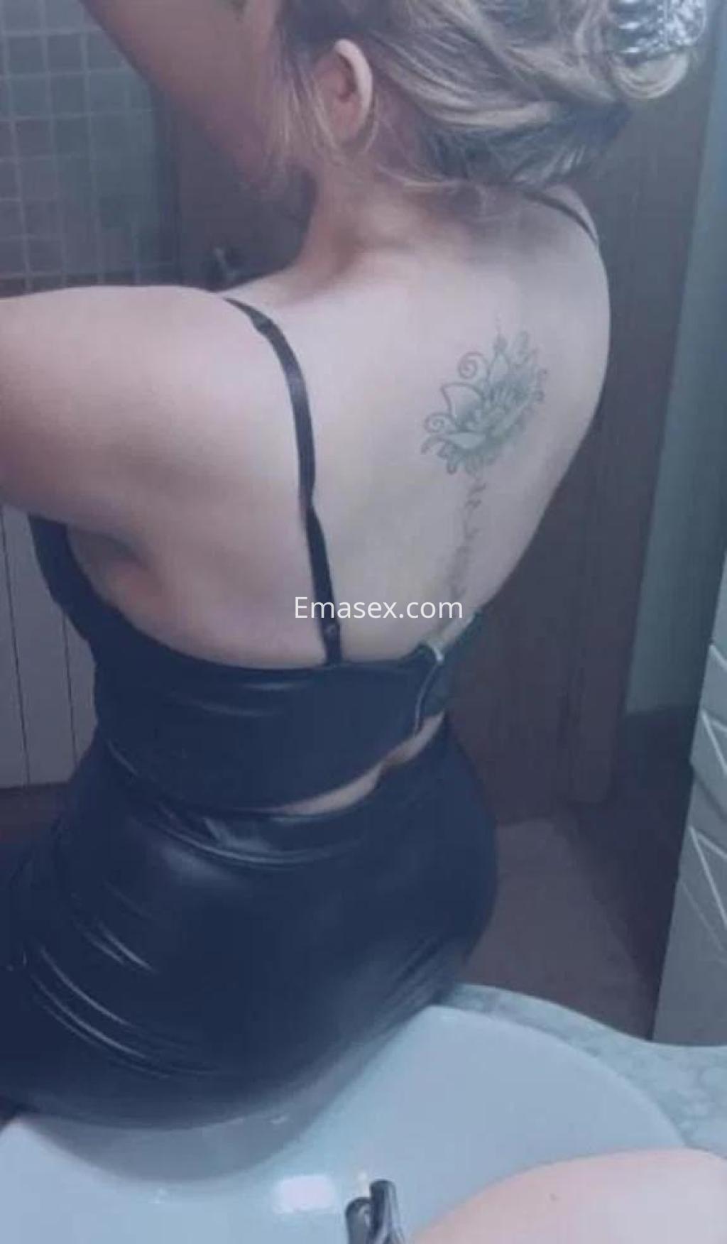 Puta en Madrid luciendo un vestido negro ajustado, con el cabello recogido y un tatuaje visible en la espalda.