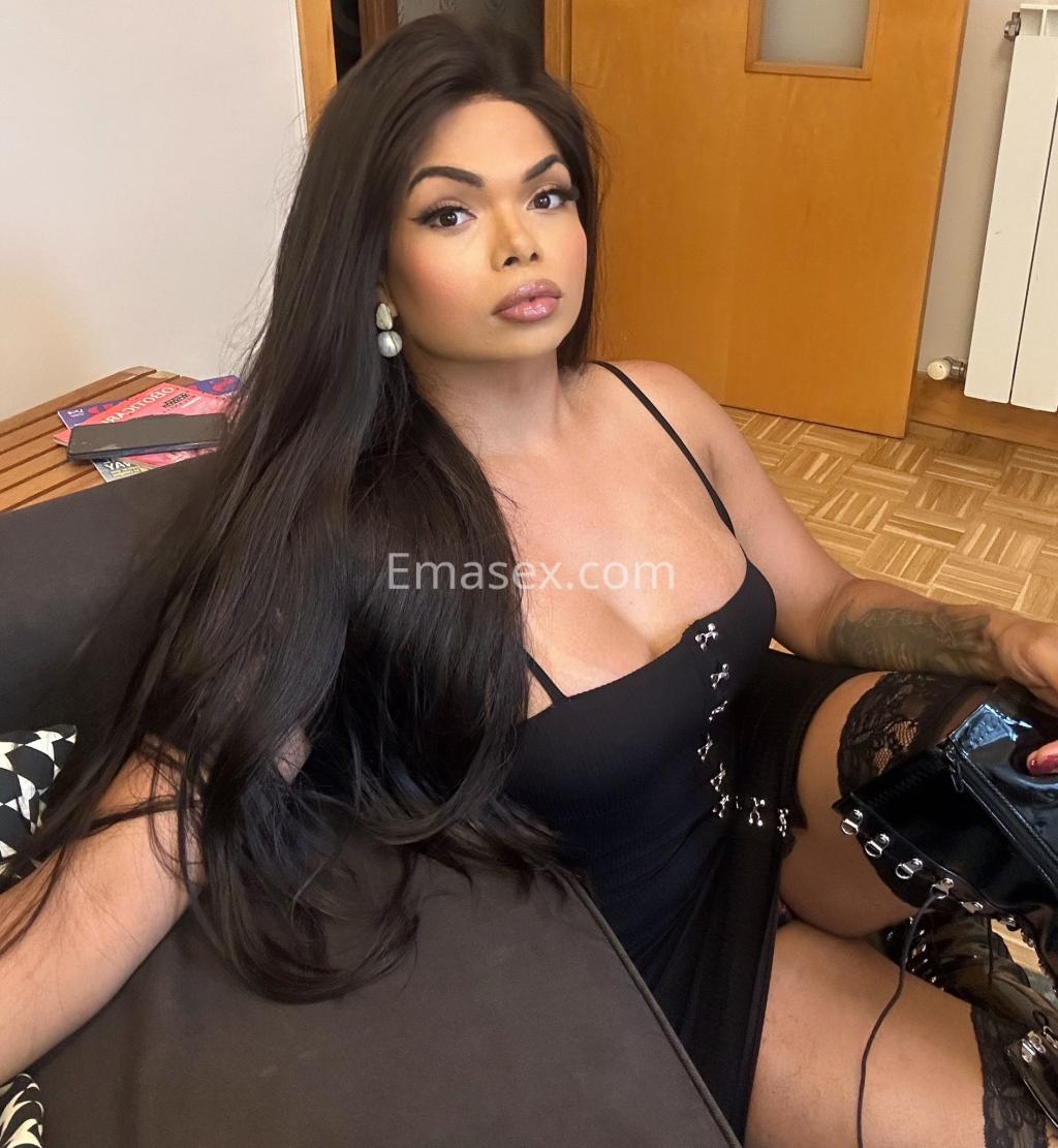 Escort trans en Bilbao con cabello largo y lacio, vestida con un vestido negro ajustado y medias de encaje.