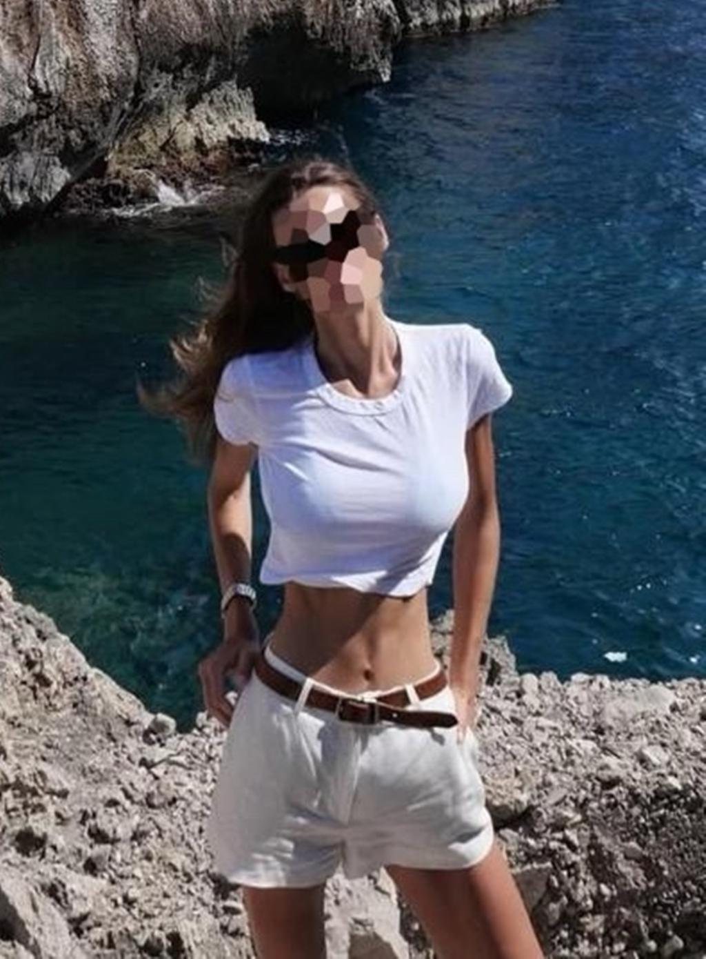 Escort en Bilbao posando al aire libre con camiseta blanca y pantalones cortos, frente al mar.