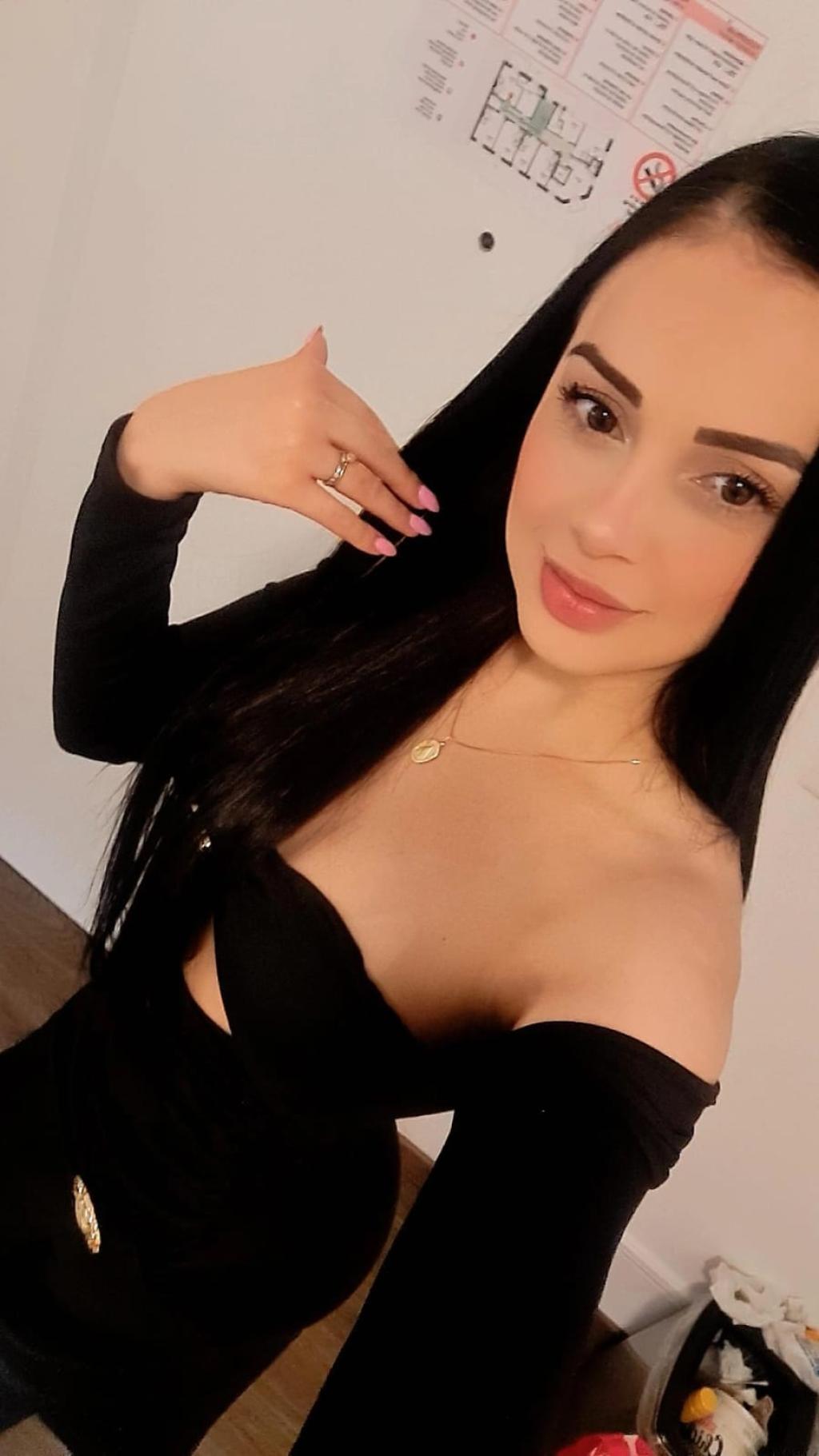 Puta con cabello largo y lacio, viste un vestido negro ajustado en Bilbao, sonriendo mientras posa.