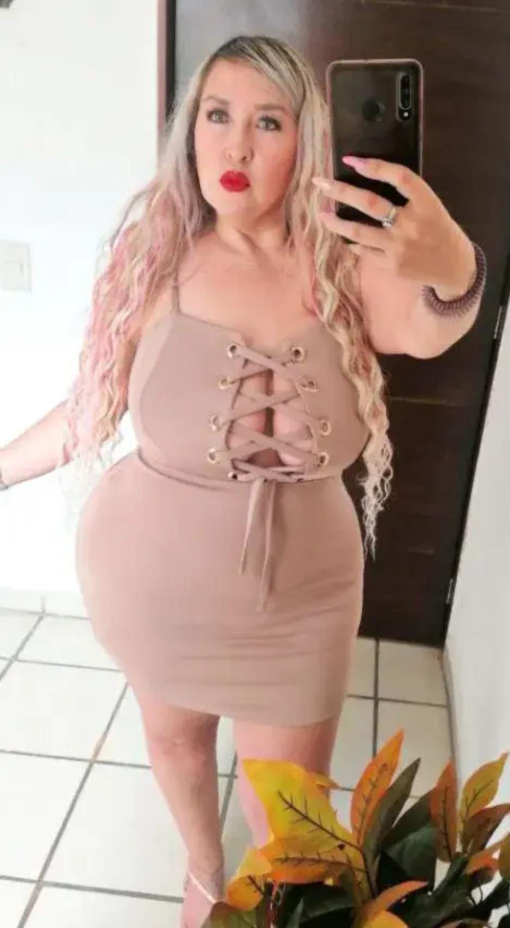 La escort en Madrid posa con un vestido ajustado de color nude con detalles de encaje, mostrando su cabello largo y ondulado.