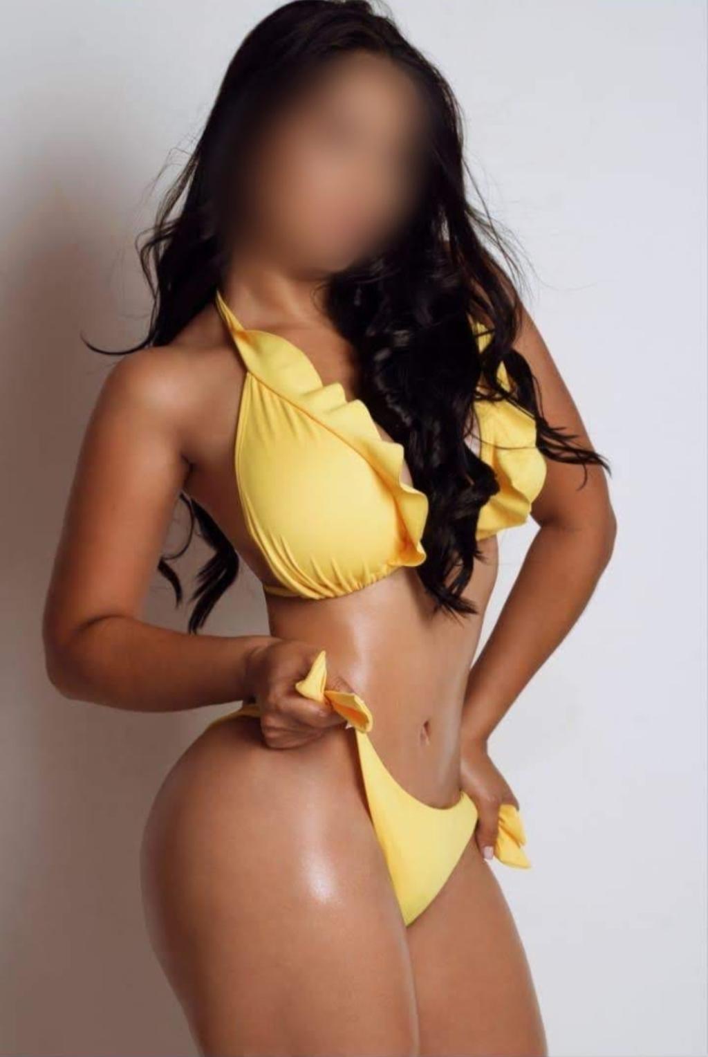 Escort en Figueres posando en bikini amarillo, con cabello largo y ondulado, mostrando una figura esculpida.