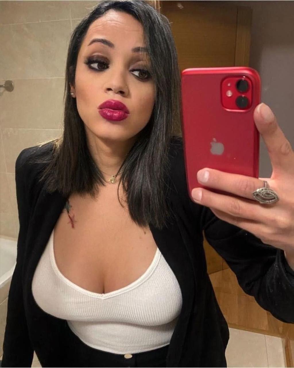 Escort trans en Pamplona, posando frente al espejo con un blazer negro y una blusa blanca, destacando su maquillaje.