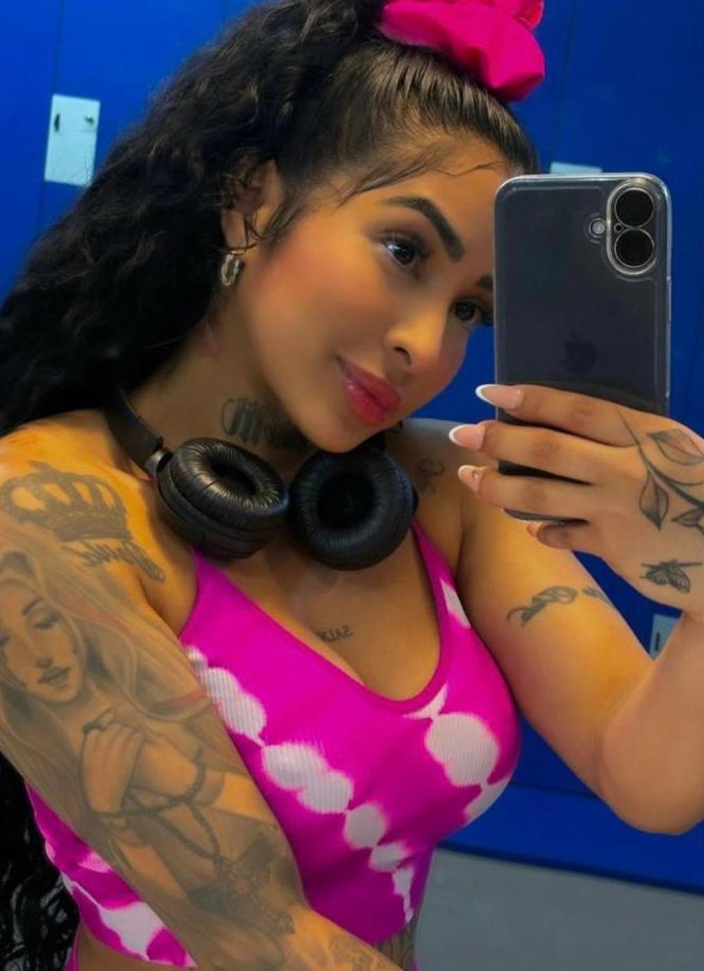 Puta tomando una selfie en Vitoria, con un top rosa, auriculares y cabello rizado, mostrando sus tatuajes.