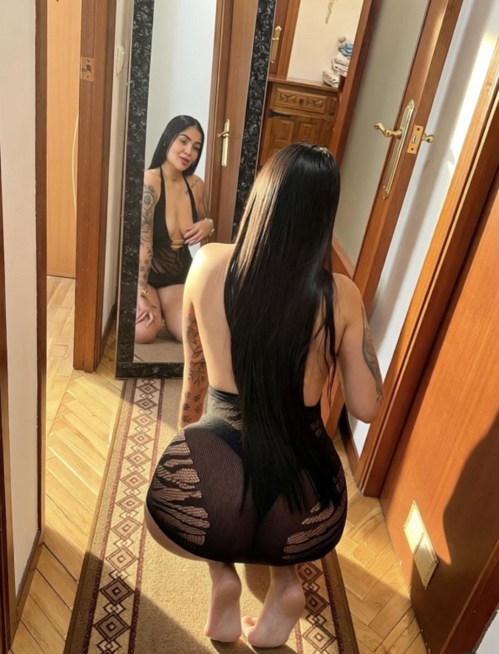 La puta de Pamplona posando de espaldas en lencería negra frente a un espejo, con cabello largo y lacio.